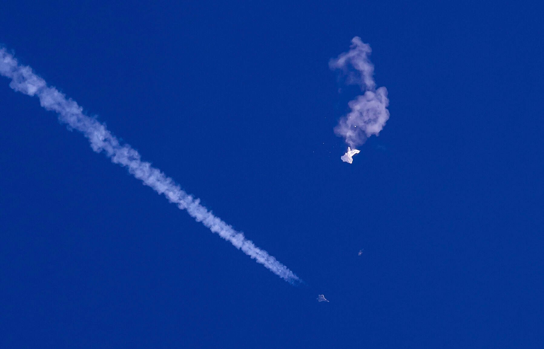 <p>In this photo provided by Chad Fish, the remnants of a large balloon drift above the Atlantic Ocean, just off the coast of South Carolina, with a fighter jet and its contrail seen below it, Feb. 4, 2023. </p>