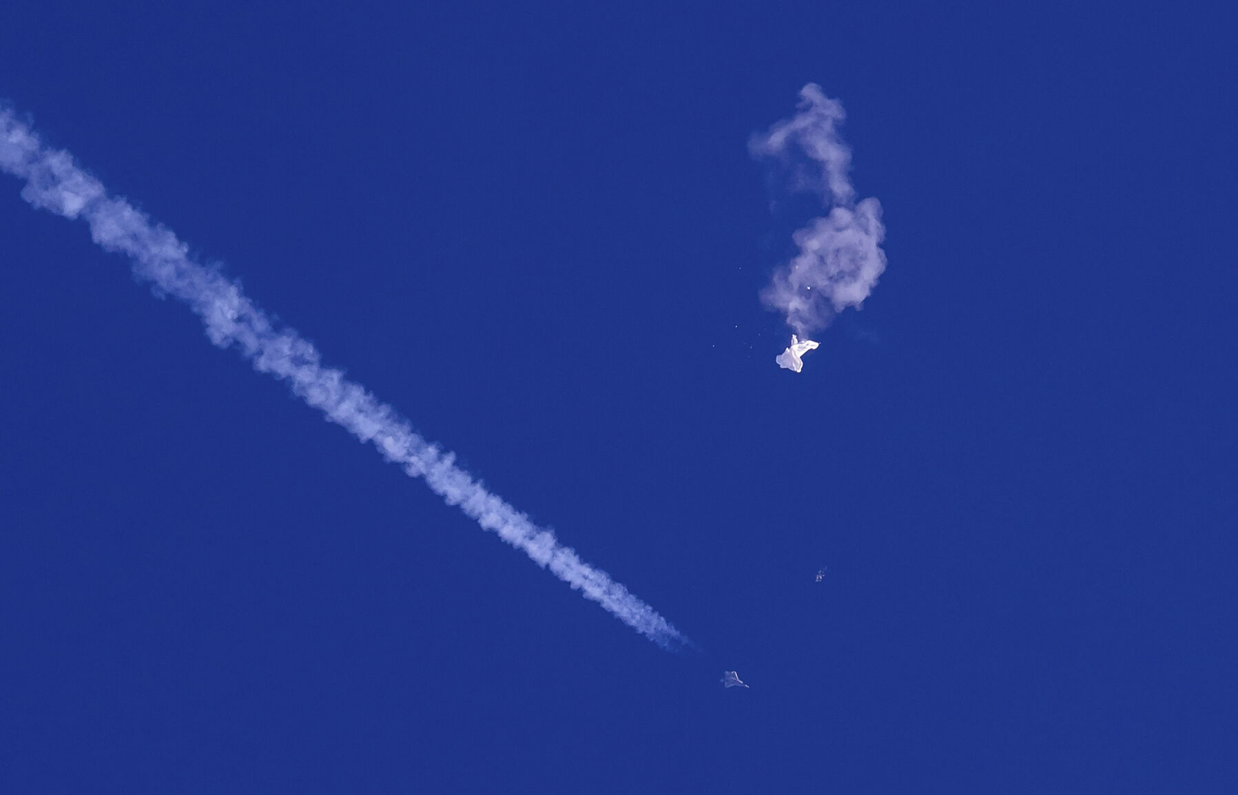 <p>The remnants of a large balloon drift Feb. 4 above the Atlantic Ocean, just off the coast of South Carolina, with a fighter jet and its contrail seen below it.</p>
