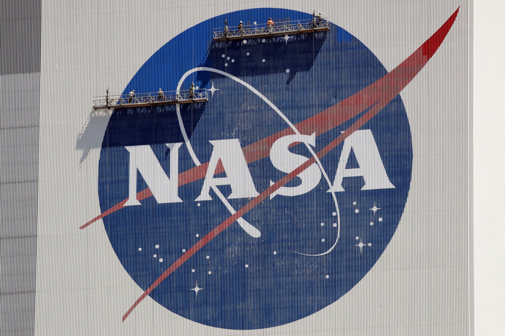 <p>FILE - Workers on scaffolding repaint the NASA logo near the top of the Vehicle Assembly Building at the Kennedy Space Center in Cape Canaveral, Fla., May 20, 2020.</p>